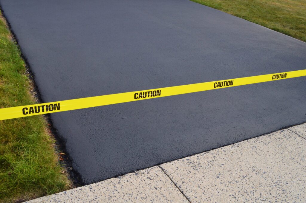 Finished result of paved seal coated blacktop driveway with caution tape.